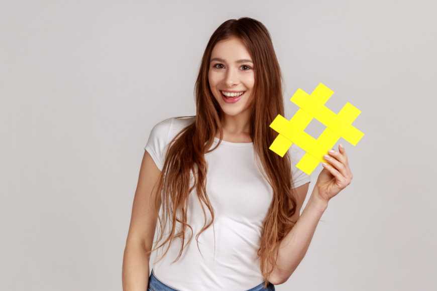 Smiling Woman Holding a Bright Yellow Hashtag Symbol